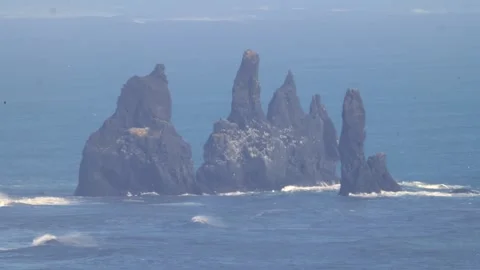 Telephoto of distant rocky cliffs off the shore of Kirkjufjara Beach Stock Footage 331762403