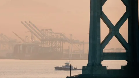 Telephoto: A Tug Sails between the massive supports of the Oakland Bay Bridge Stock Footage 94239647