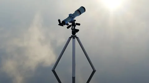 Telescope standing on a reflective (mirror) surface on a cloudy sky background Video stock 307054605