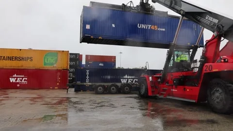 Telescopic container handler lowering steel container onto articulated lorry Stock Footage 258229818
