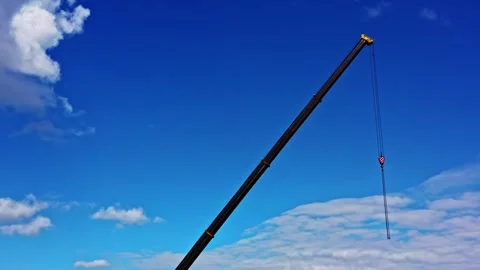 Telescopic crane boom with hook extended high against bright blue sky and clouds Stock Footage 323379515