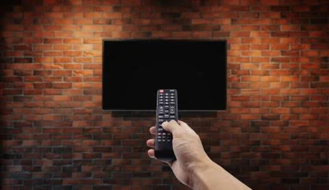 Television on brick wall with hand using remote control Stock Photos