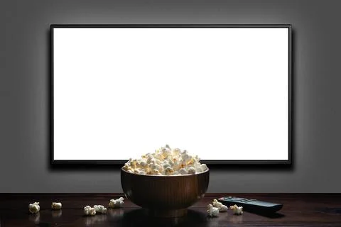 Television on a gray wall with remote control and popcorn bowl on the table.  Stock Photos