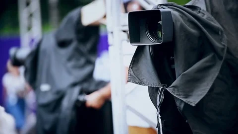 Television news camera on a tripod protected by a black rain cover 스톡 동영상 78098673