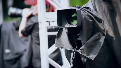 Television news camera on a tripod protected by a black rain cover 스톡 동영상 78098724