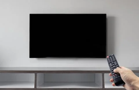 Television on white wall with hand using remote control Stock Photos