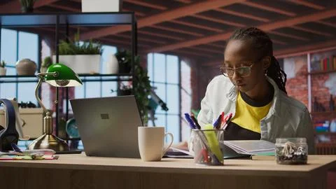 Teleworker in apartment reading documents on notebook and taking notes Stock Photos