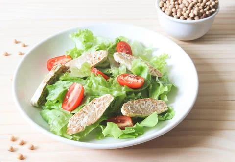 Tempeh or tempe salad with tomato and green vegetable in white plate and a bo Stock Photos
