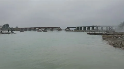 Temporary ferry carrying tractor crossing a river near a damaged bridge Stock Footage 330567440