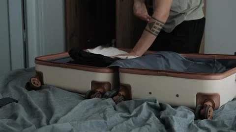 Temporary living and relocation. Close up of hands packing clothes into suitcase Видео 346251894