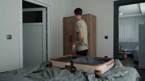 Temporary living and relocation. Man packing clothes into suitcase in rented Vídeo Stock 346253921