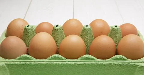 Ten rustic brown eggs lie in cardboard boxes on a white wooden table Stock Photos