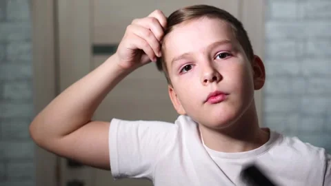 Ten year old boy combing his hair standing in front of a mirror looking at the c Stock Footage 306355601