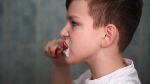 A ten year old boy is concentrating on brushing his teeth with a red toothbrush Video stock 306355192