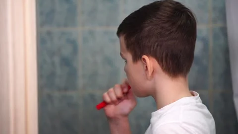 A ten year old boy is concentrating on brushing his teeth with a red toothbrush Stock Footage 306355306