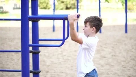 A ten-year-old boy does somersaults on the horizontal bars in the park. Stock Footage 248714819