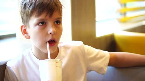 A ten-year-old boy drinks a cold drink through a straw while sitting at the tabl Stock Footage 248378470