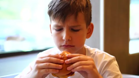 A ten-year-old boy eats a burger sitting at the table. going to a cafe. Stock Footage 248378822