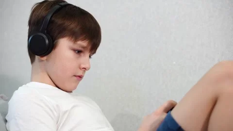 Ten year old boy lying on the couch playing on smartphone with wireless headphon Stock Footage 297553391