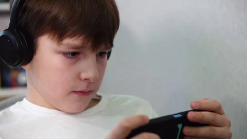 Ten year old boy lying on the couch playing on smartphone with wireless headphon Stock-Footage 297553542