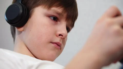 Ten year old boy lying on the couch playing on smartphone with wireless headphon Stock Footage 297553573