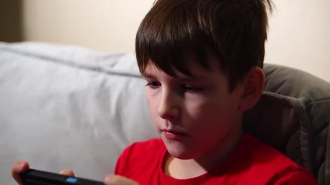 Ten year old boy playing smartphone sitting on sofa Stock Footage 297451414