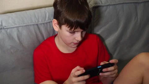 Ten year old boy playing smartphone sitting on sofa Video stock 297451427