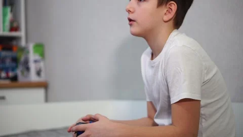 Ten year old boy playing game console sitting on bed Stock Footage 297553120