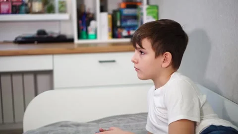 Ten year old boy playing game console reclining on bed Stock Footage 297553156