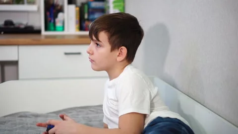 Ten year old boy playing game console reclining on bed Stock Footage 297553176