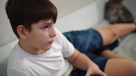 Ten year old boy playing game console reclining on bed Stock Footage 297553207
