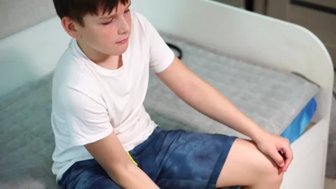 Ten year old boy pumping biceps with green dumbbell sitting on bed. Stock-Footage 307023205
