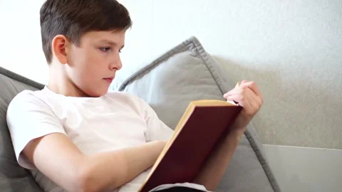 Ten year old boy reading a book lying on his bed in his room Stock Footage 306355479