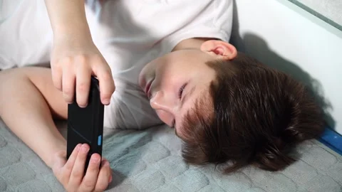 A ten-year-old boy in a white T-shirt is enthusiastically playing on his phone w Stock Footage 306445366