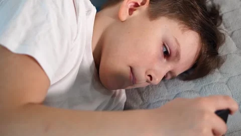 A ten-year-old boy in a white T-shirt is enthusiastically playing on his phone w Stock Footage 306445379