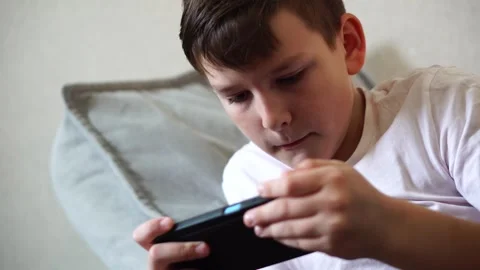 A ten-year-old boy in a white T-shirt enthusiastically plays on his phone while  Video stock 306445389
