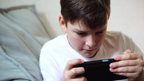 A ten-year-old boy in a white T-shirt enthusiastically plays on his phone while  Stock Footage 306445402