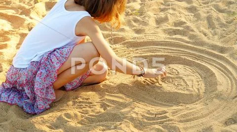 Ten year-old girl drawing a odd face on the sand Stock Photos