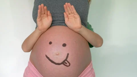 Ten-yearold boy playing with his pregnant moms belly painted with a smiley face Stock Footage 312114190