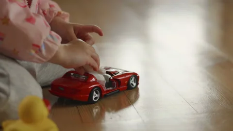 Tender childs hands playing with red car model and tiny teddy on wooden floor Stock Footage 157106136