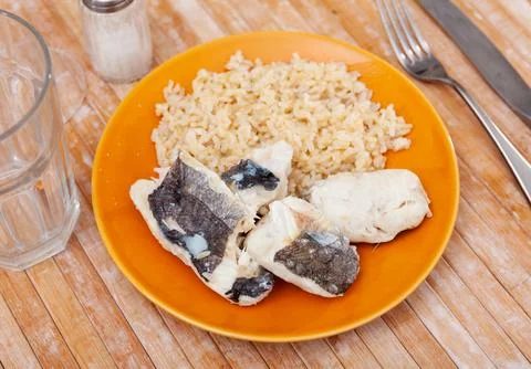 Tender meat of baked cod fillet is garnished with boiled basmati rice. Stock Photos