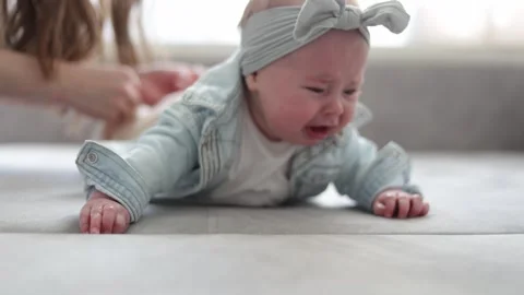 Tender moment of a baby learning to crawl on a soft surface with parent's gentle Stock Footage 340580982