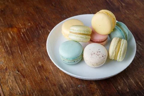 Tender multicolored macaroons with different tastes on white plate, wooden Stock Photos