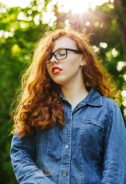 Tender red haired young model in glasses posing in rays of sun at the park Stock Photos