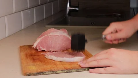 Tenderizing raw pork cutlet with meat mallet on wooden cutting board in kitchen. Stock Footage 317154106