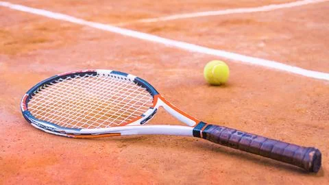 Tennis racket lying next to a ball on a court Stock Photos