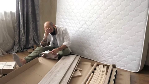 A tense man with paper instructions for assembling furniture is going to Stock Footage 203934275