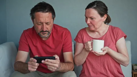 Tense middle-aged couple avoid eye contact on a couch at home; man focused .. Stock Footage 336257330