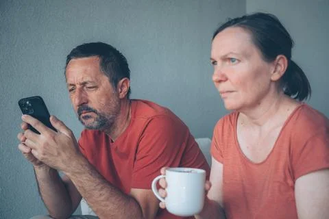Tense middle-aged couple avoid eye contact on a couch at home; man focused .. Stock Photos