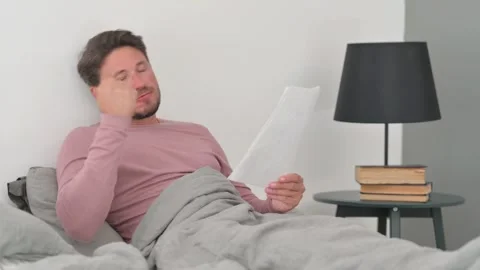 Tense Middle Aged Man Shocked while Reading Report in Bed 스톡 동영상 287405906